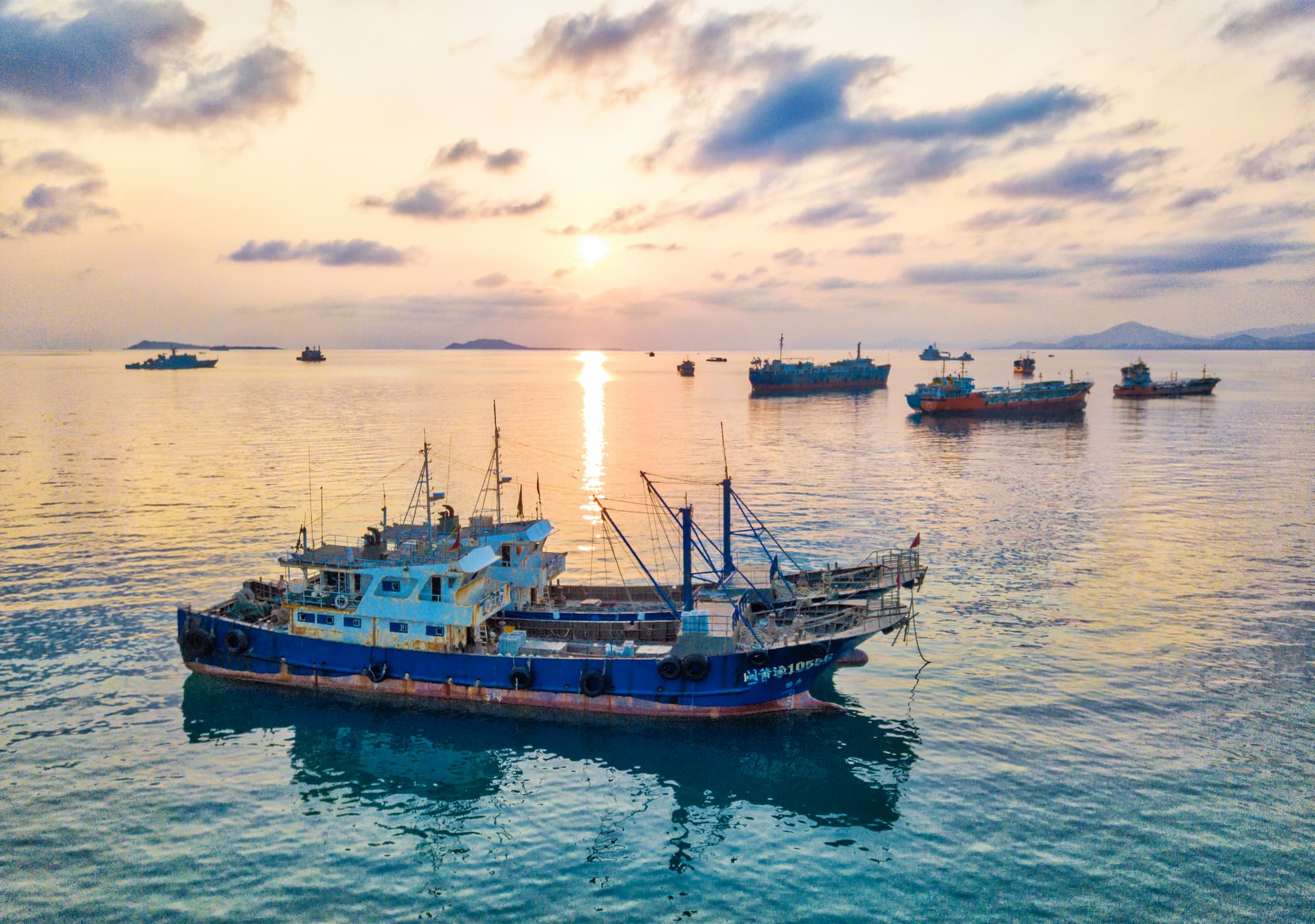 Boats anchored in the ocean as the sun sets