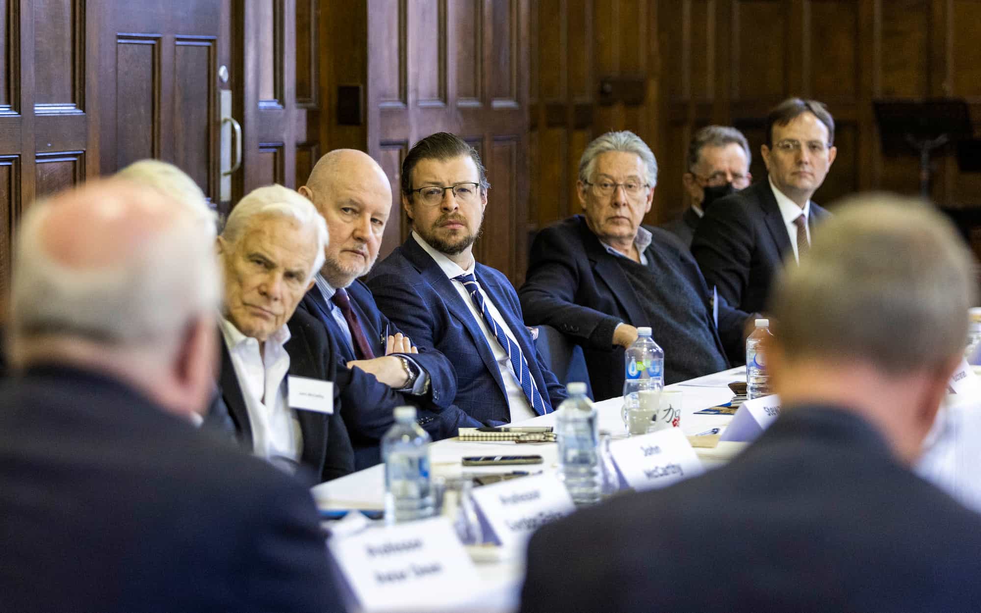 A group of men seated around a long table, engaged in a discussion