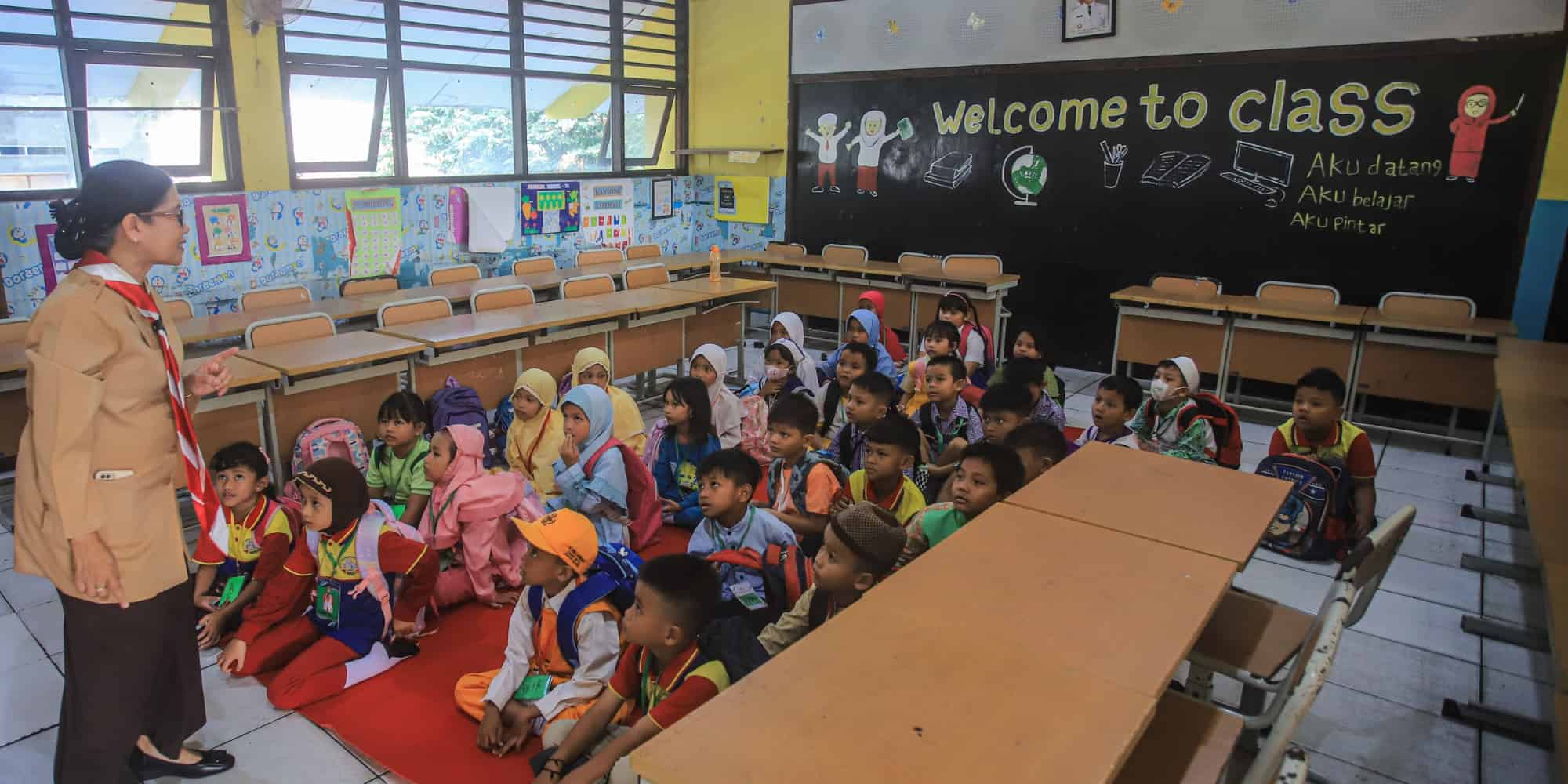 A teacher stands in front of a classroom, engaging with a group of attentive children