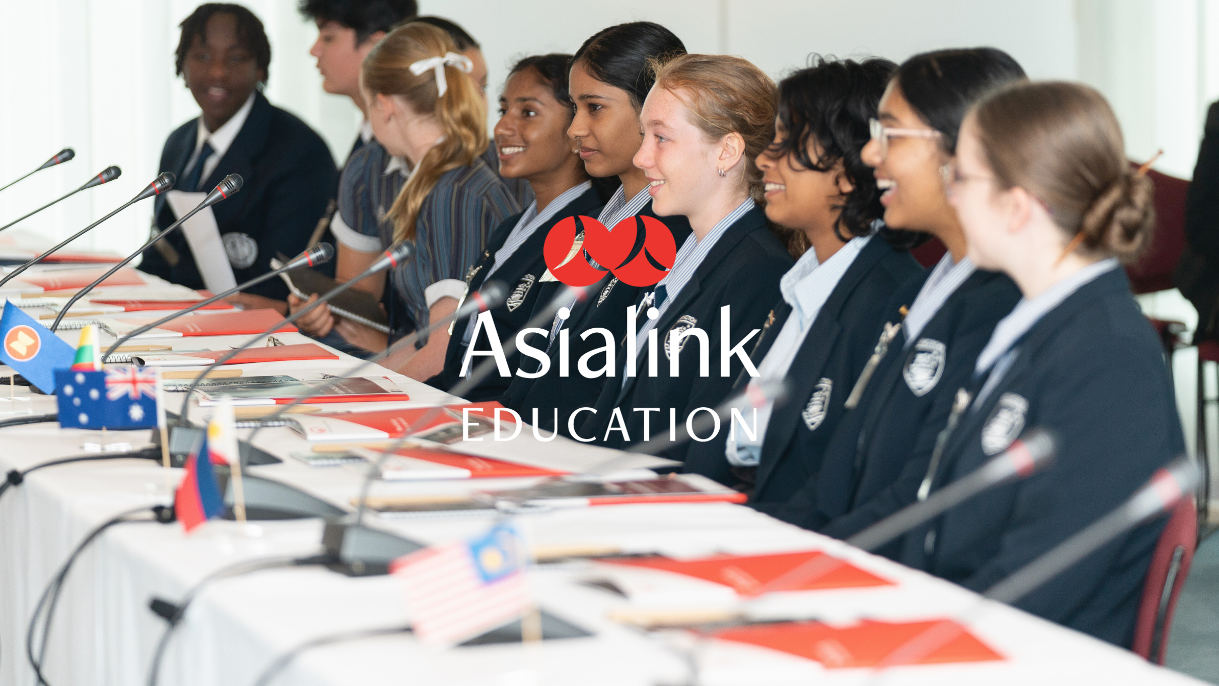 Group of students sit at a conference table with international flags and microphones.