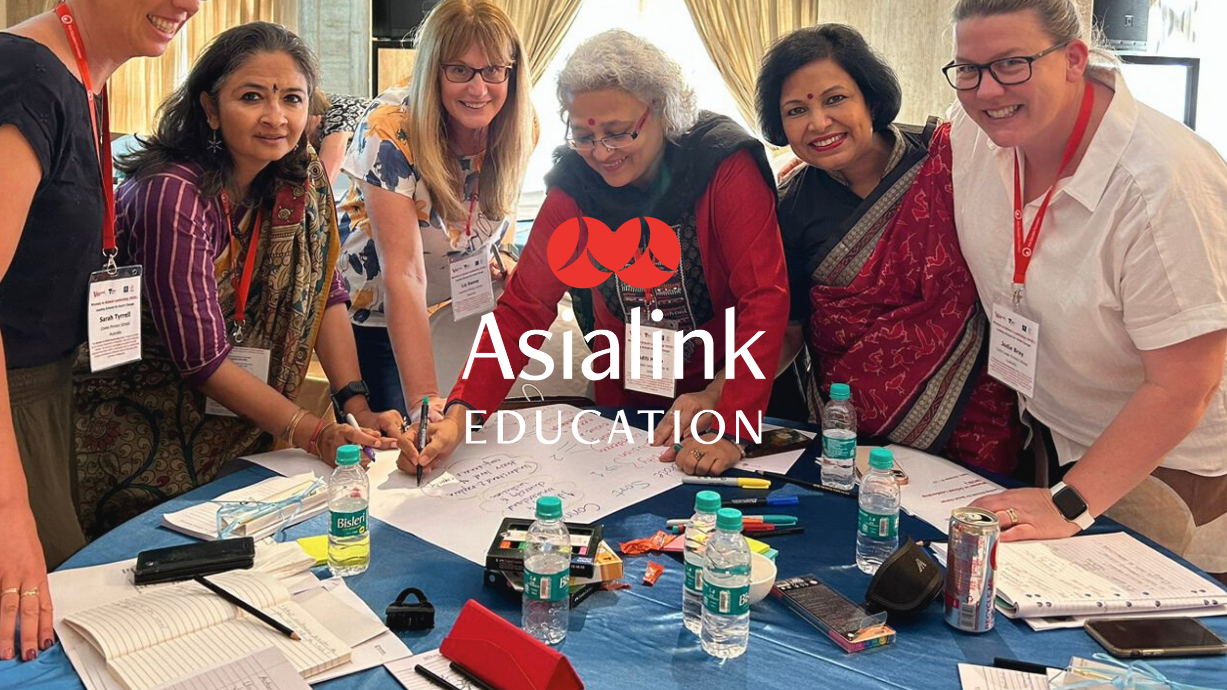 A group of women are gathered around a table, smiling and engaged in discussion.