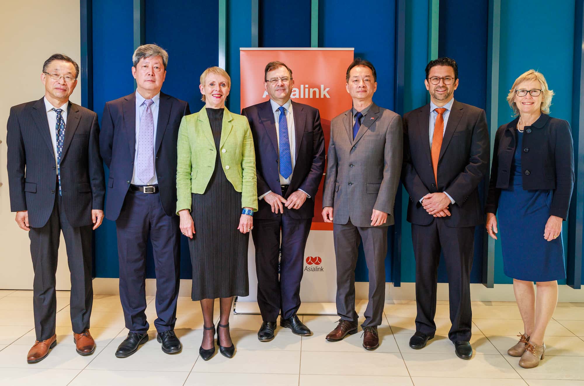 A group of business professionals stands in front of a banner