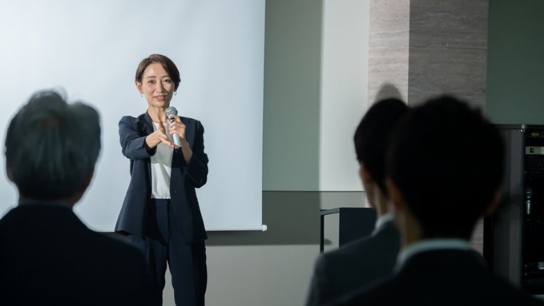 An asian woman in professional attire speaks in front of audience