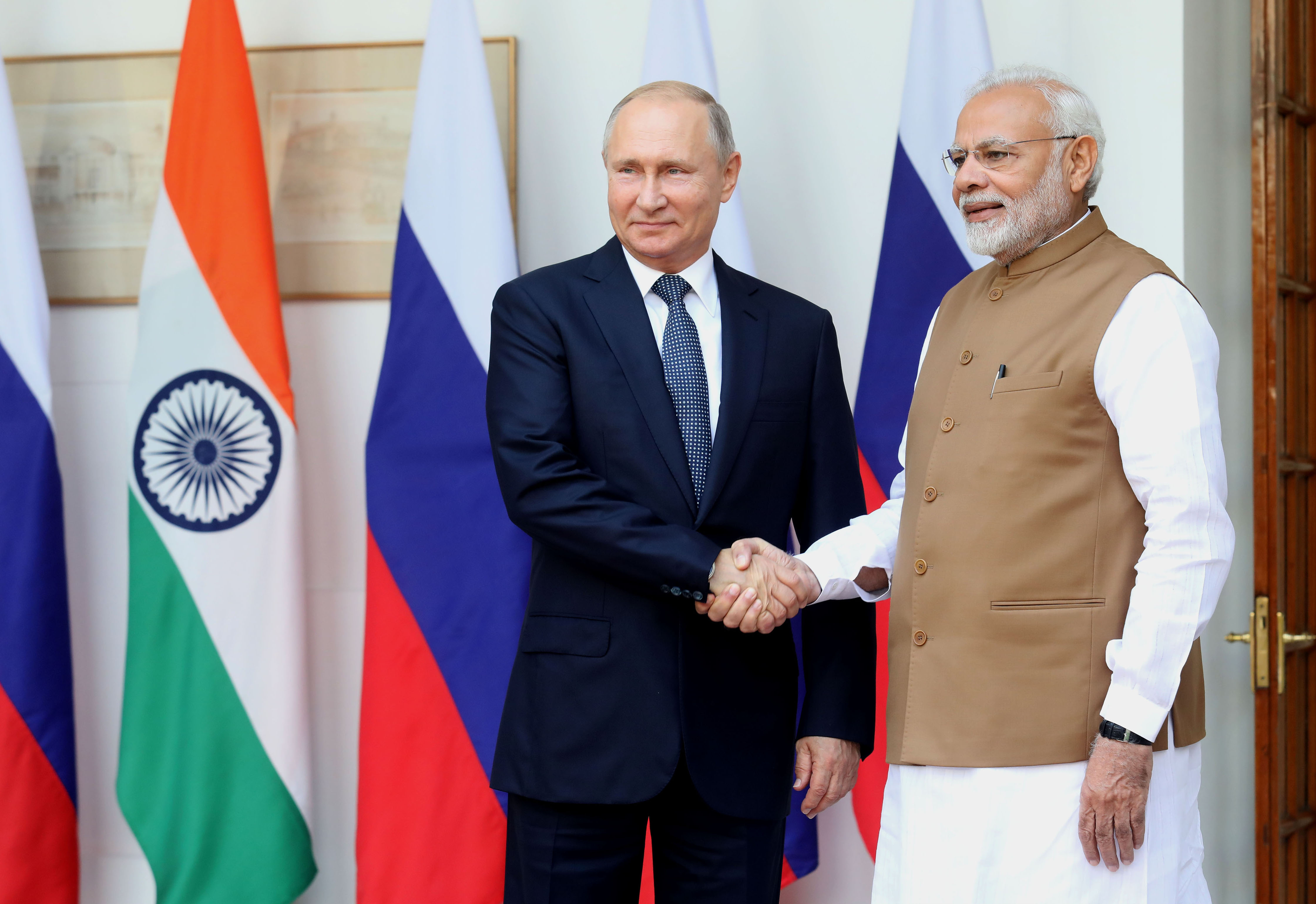 Vladimir Putin and Narendra Modi stand and shake hands in front of Indian and Russian flags