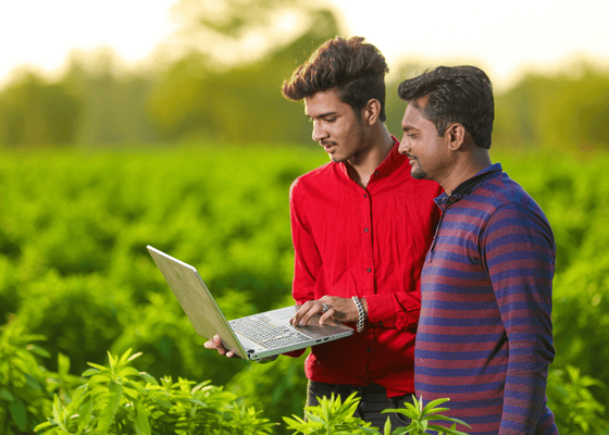 Two men looking at a laptop screen in a field
